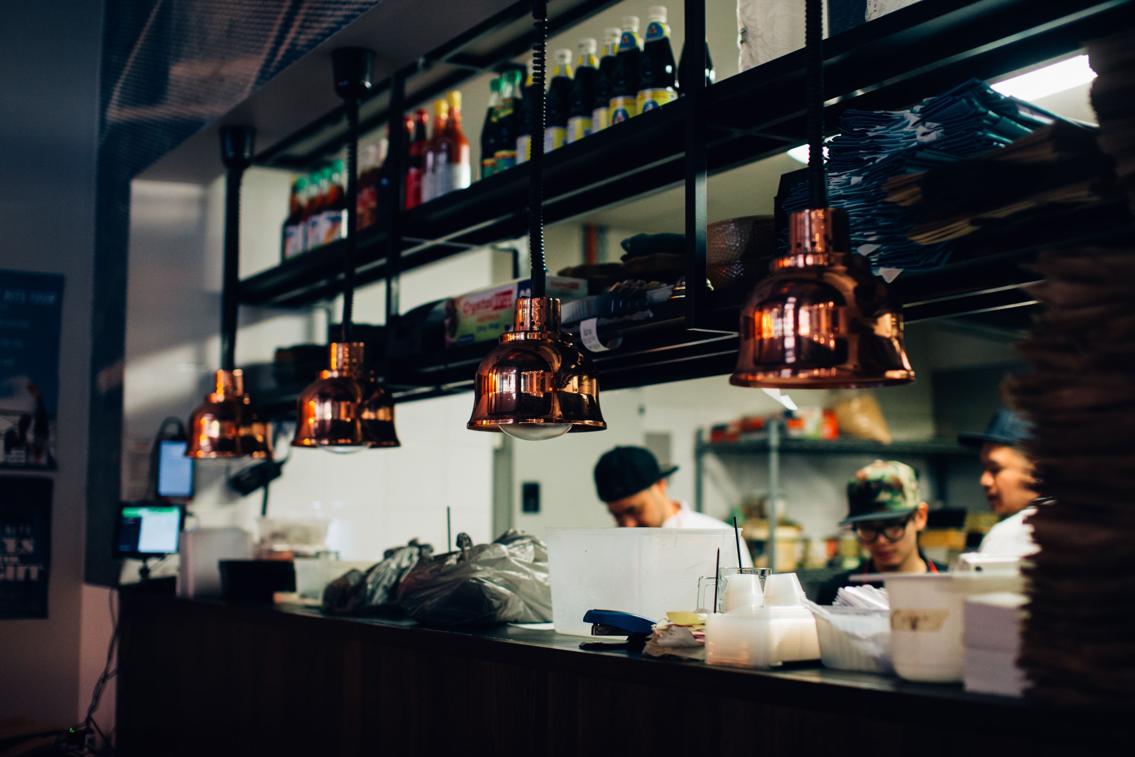 Personal preparando pedidos en una cocina de restaurante bajo lámparas colgantes